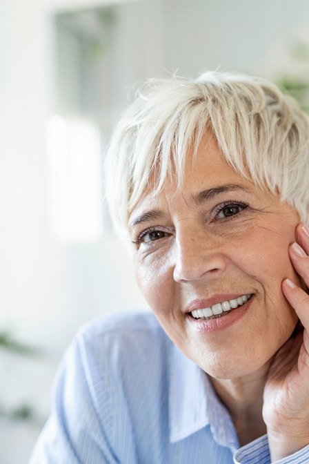 A woman in her fifties with healthy skin touching her face, representing menopausal skin care at Florida Aesthetics and Wellness